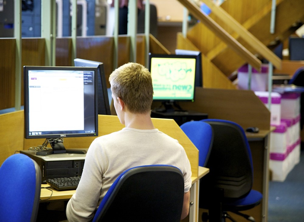 Image of male student sat in front of a computer workstation.