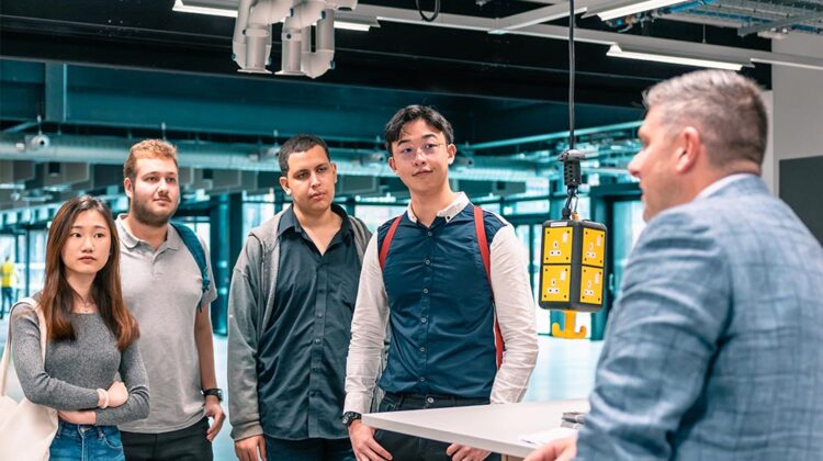 A member of staff speaking to four students while stood in one of the MECD practical teaching spaces