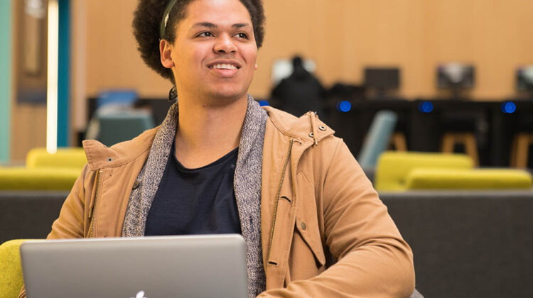 Picture of student working on a laptop, smiling at something off camera