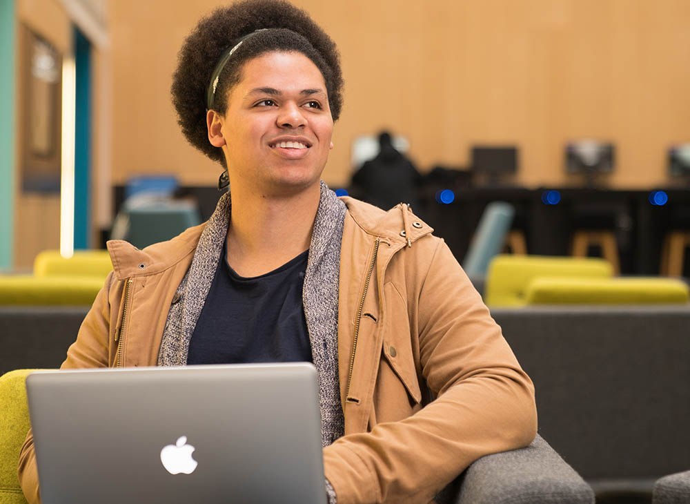Picture of student working on a laptop, smiling at something off camera