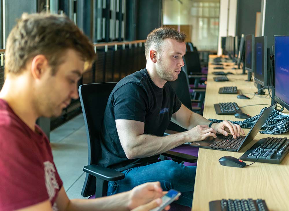 Two students working on a desk on individual PC's in MECD